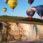 AI generated image of hot air balloons flying over cliff which has The Bees carved into it