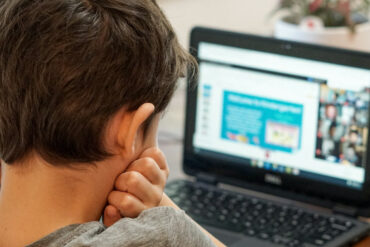 Young boy sitting at the dinner table working on his laptop