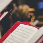 christmas lights in the background of hymn song sheets held in red folders