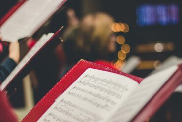 christmas lights in the background of hymn song sheets held in red folders