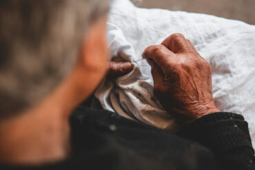 older person embroidering onto a white shirt by elio santos