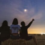 three people sat on hale bales in a field looking at the stars