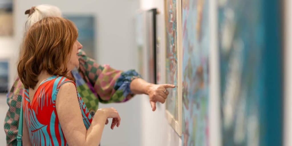 two women looking at art on a gallery wall during open studios event