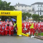 Children and adults dressed as santas, waiting at the start line of the Santa Dash race