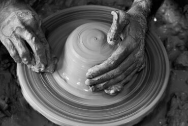 black and white photo of person throwing clay on a potters wheel