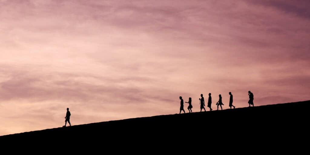 silhouettes of people walking along the ridge of a hill with pink sky in the background