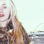 woman with leopard skin fluffy jacket on sitting next to guitar AMP