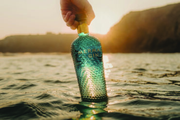 person holding a bittle of mermaid gin in the sea