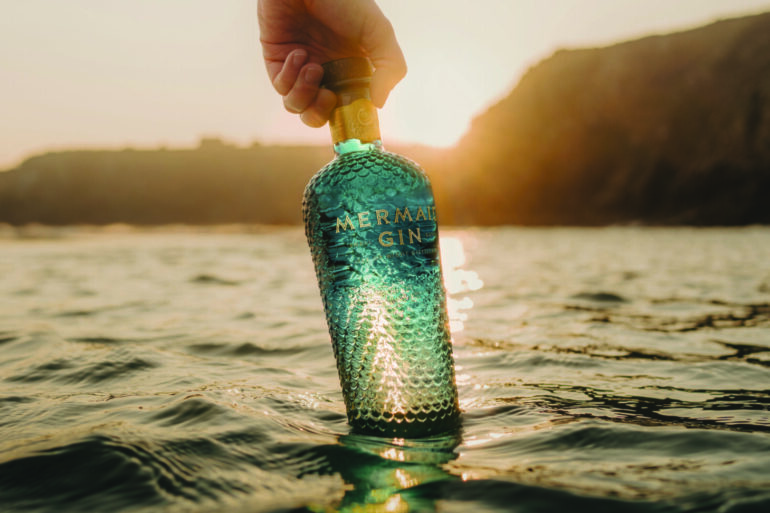 person holding a bittle of mermaid gin in the sea