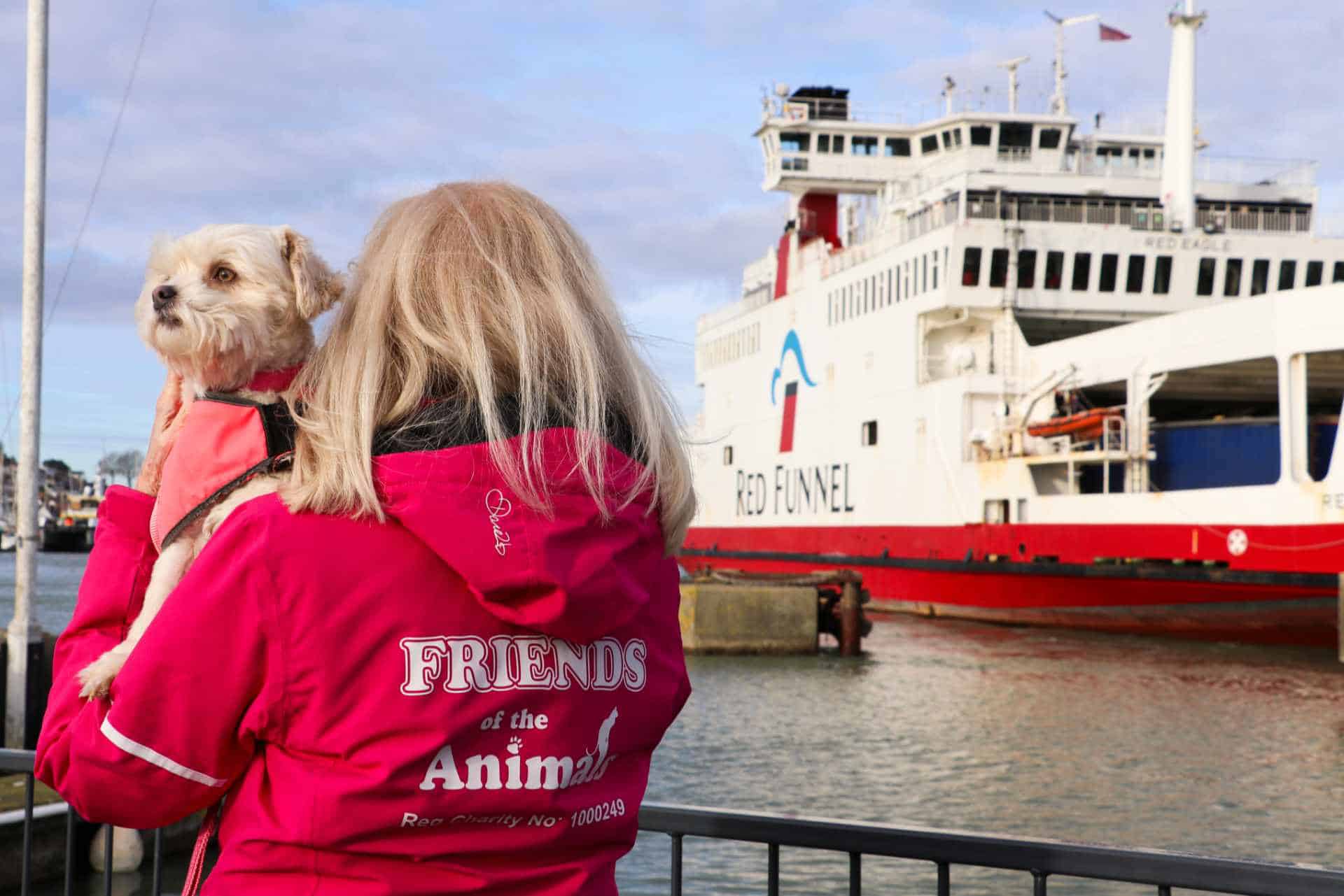 Person holding a dog at ferry port, with ferry in the background