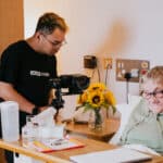 Older woman in hospice bed with grandchild next to her bed and man filming them together