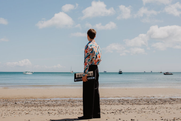 Thomas Luke standing on a beach with an electric keyboard