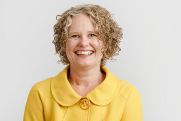becky mcgregor portrait against a plain white background, showing Becky wearing a yellow jacket and smiling at the camera