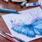 butterfly painting on a table surrounded by paints, palette and brushes