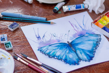 butterfly painting on a table surrounded by paints, palette and brushes