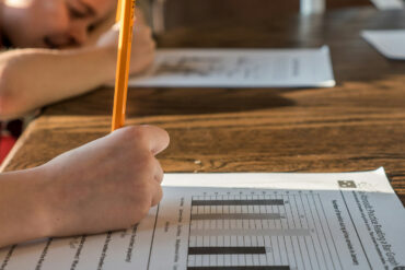two children filling in worksheets at a dining room table