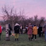 People standing around a tree at sunrise performing a wassail