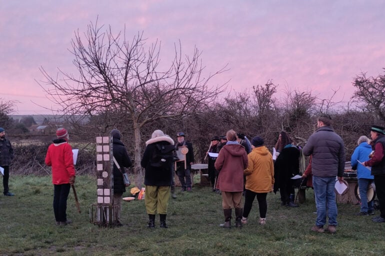 People standing around a tree at sunrise performing a wassail