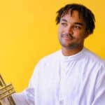 Aaron Azunda Akugbo against a yellow background holding his trumpet