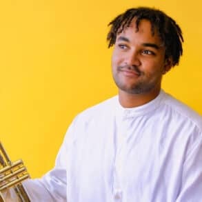 Aaron Azunda Akugbo against a yellow background holding his trumpet