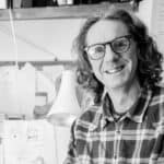 black and white photo of Neal Layton smiling at the camera whilst standing by his drawing board