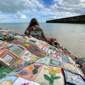 Person wearing the coat of hopes on a beach, with people holding up the coat tails