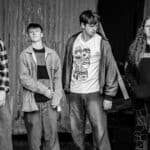 Black and white photo of thesis band members standing in a line looking at the camera