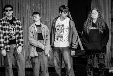 Black and white photo of thesis band members standing in a line looking at the camera