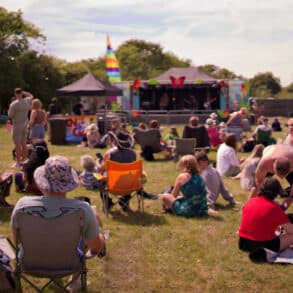 People sitting on the gras or on fold up chairs watching performers on the stage at Three Rivers Music Festival