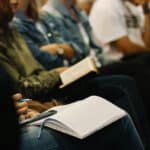 people in a conference audience taking notes
