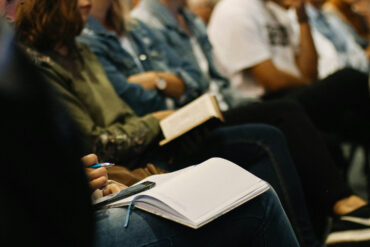 people in a conference audience taking notes