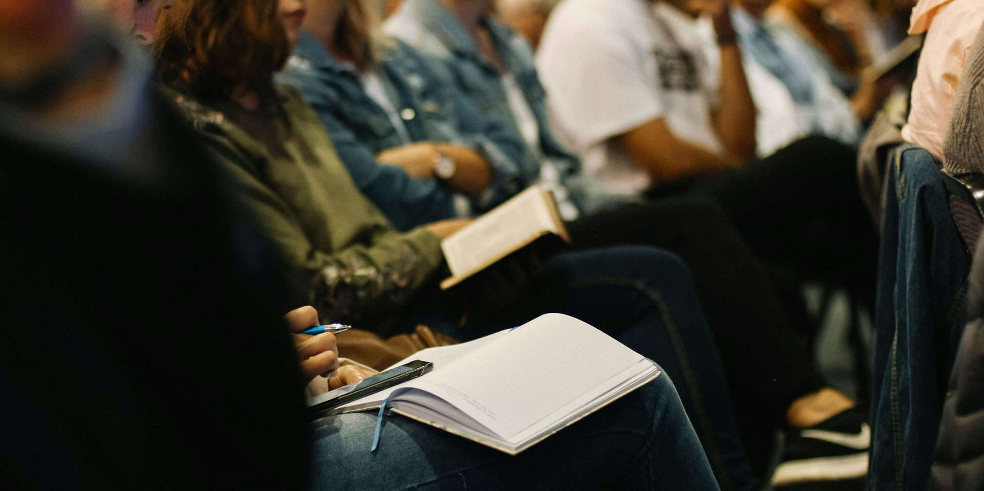 people in a conference audience taking notes