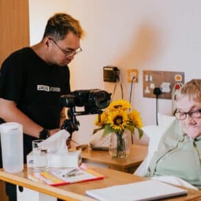 Man filming a woman in bed writing a letter