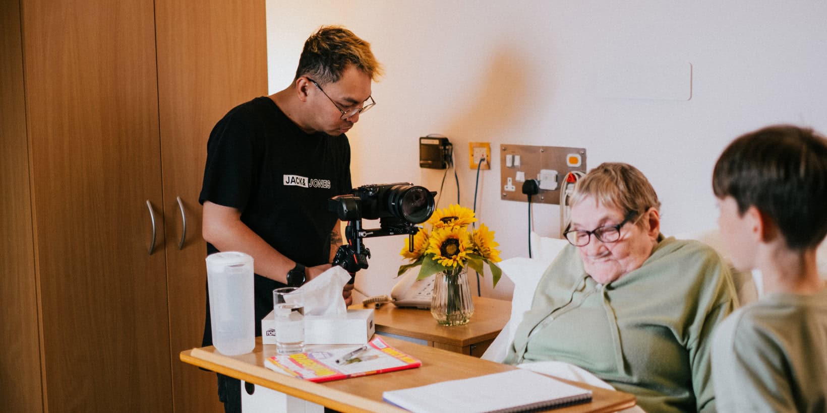 Man filming a woman in bed writing a letter