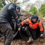 Person filming a man climbing out of a large plastic tube at robin hill country park in jan 2024