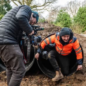 Person filming a man climbing out of a large plastic tube at robin hill country park in jan 2024