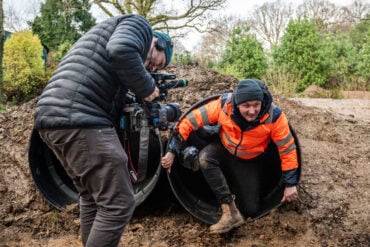 Person filming a man climbing out of a large plastic tube at robin hill country park in jan 2024