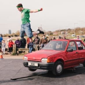 Man jumping off a car with audience standing around