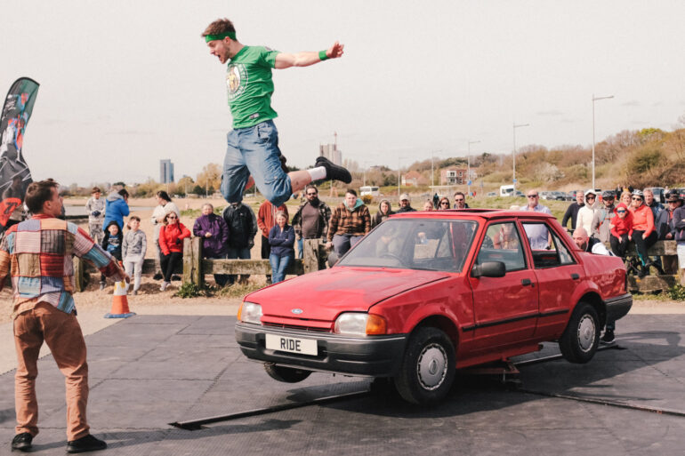 Man jumping off a car with audience standing around