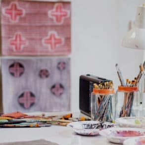 artists studio with paintbrushes in pots and painted fabric on the walls