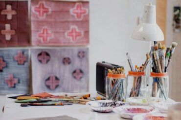 artists studio with paintbrushes in pots and painted fabric on the walls