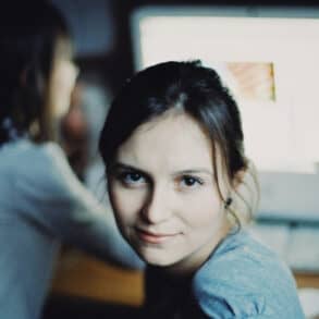 two woman sat at a computer with one looking into the camera by alexey demidov