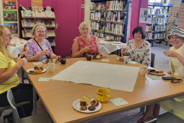 Bake off ladies sitting at tables in the library with their cakes