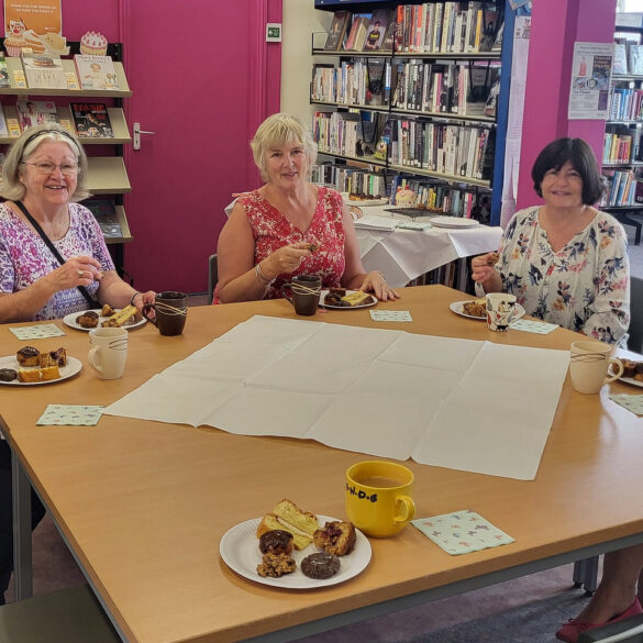 Bake off ladies sitting at tables in the library with their cakes