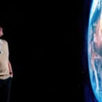 Chris packham looking at a large projection of earth from space