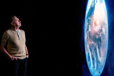 Chris packham looking at a large projection of earth from space