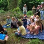 children sitting on blankets in woods listening to a storyteller