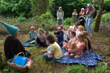 children sitting on blankets in woods listening to a storyteller