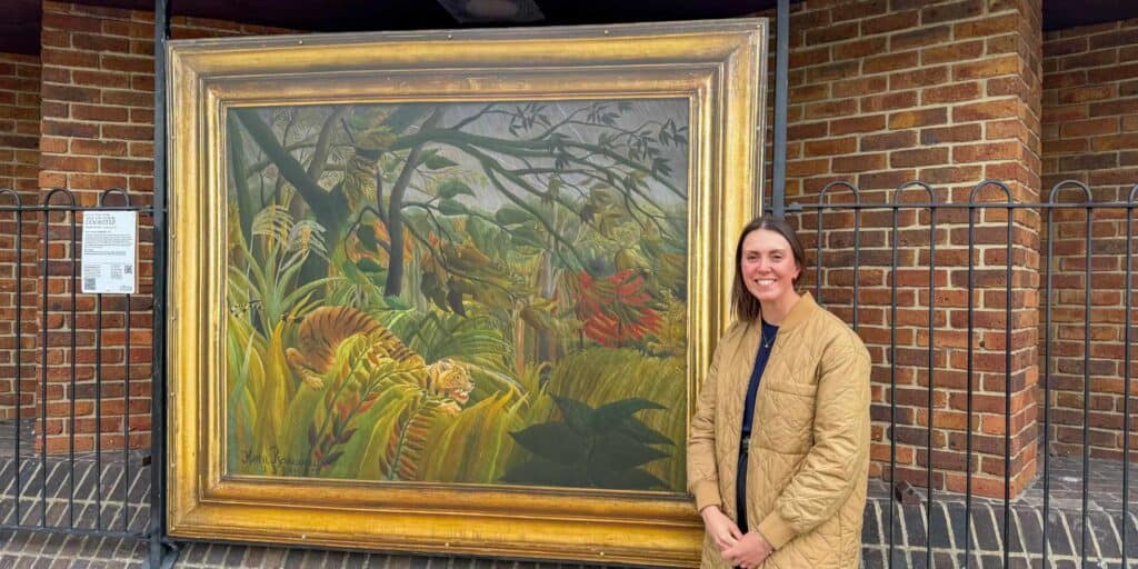 The National Gallery’s Head of Exhibitions, Alex Kavanagh, standing in front of Surprised! by Henri Rousseau at Newport Bus Station