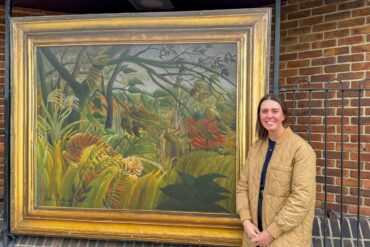 The National Gallery’s Head of Exhibitions, Alex Kavanagh, standing in front of Surprised! by Henri Rousseau at Newport Bus Station
